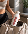 Load image into Gallery viewer, Person holding a white water bottle with a pink accent, opening a beige bag.
